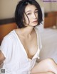 A woman sitting on top of a bed in a white shirt.