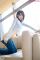 A woman sitting on top of a white couch next to a window.