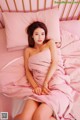 A woman in a pink dress sitting on a bed.